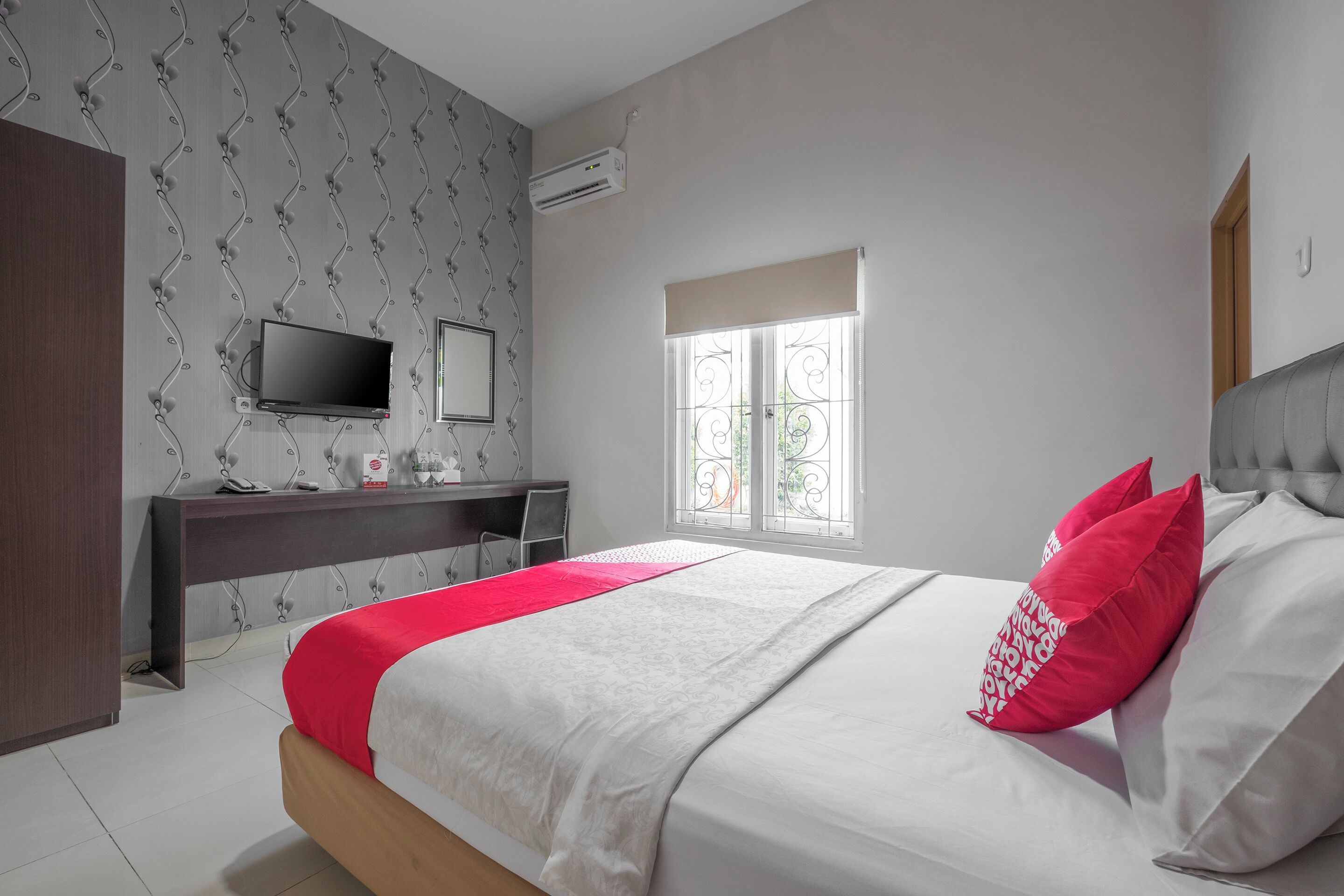 A bedroom with a bed, a desk, a TV, and a window.