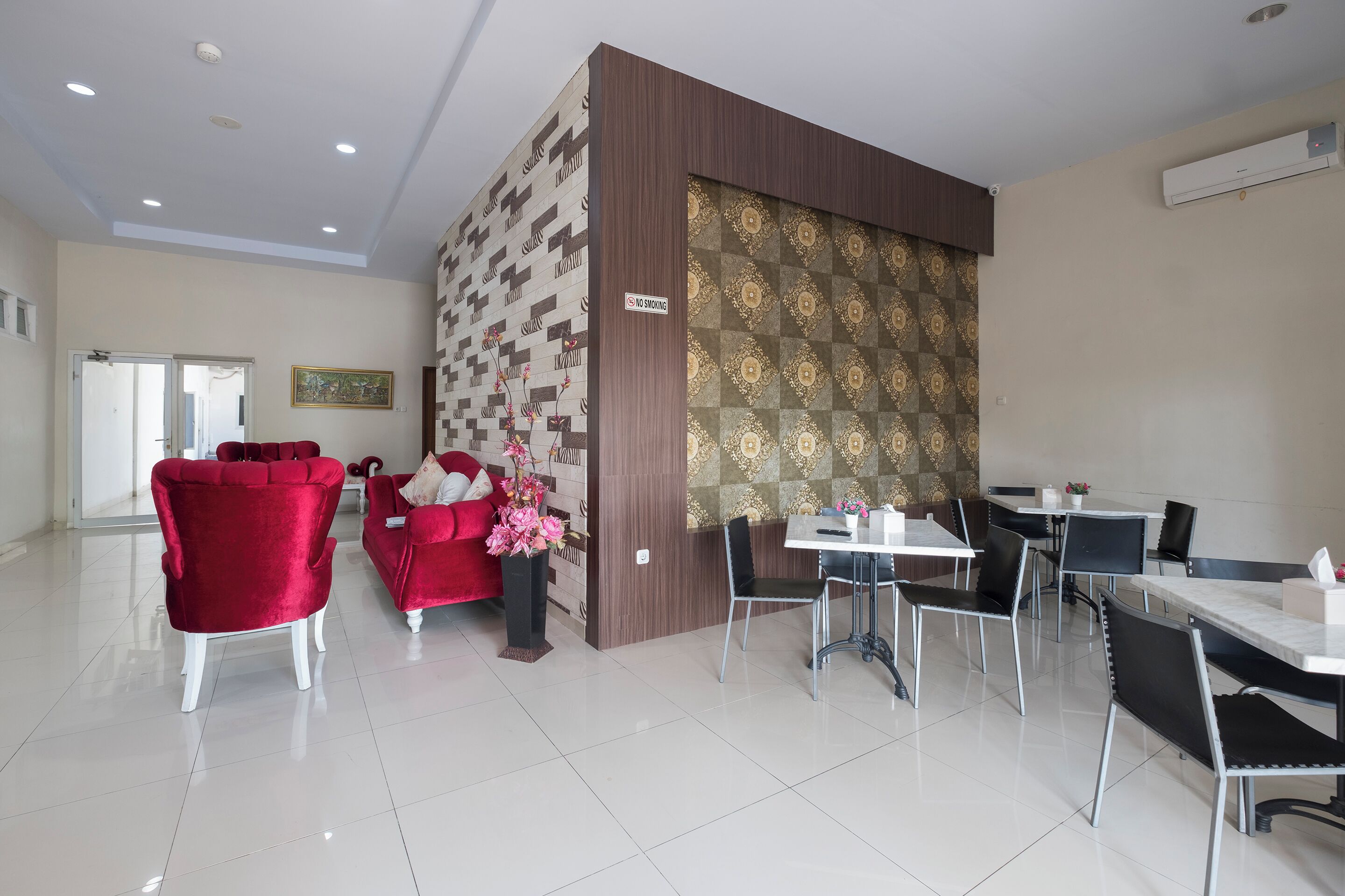 A hotel lobby with a modern design, featuring a red velvet sofa, a black chair, and a dining area with tables and chairs.