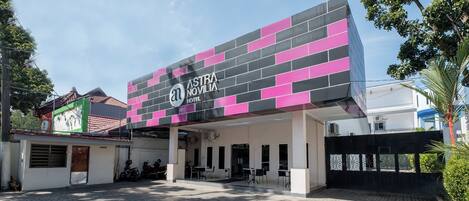 A hotel entrance with a modern facade, a covered outdoor seating area, and a paved driveway.