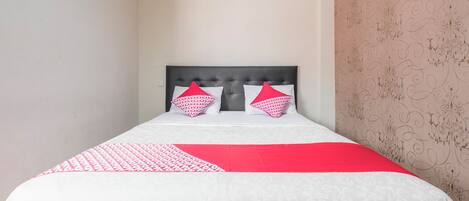 A neatly made bed with a patterned bedspread and two pillows, a red and white color scheme, and a decorative wall with a floral pattern.