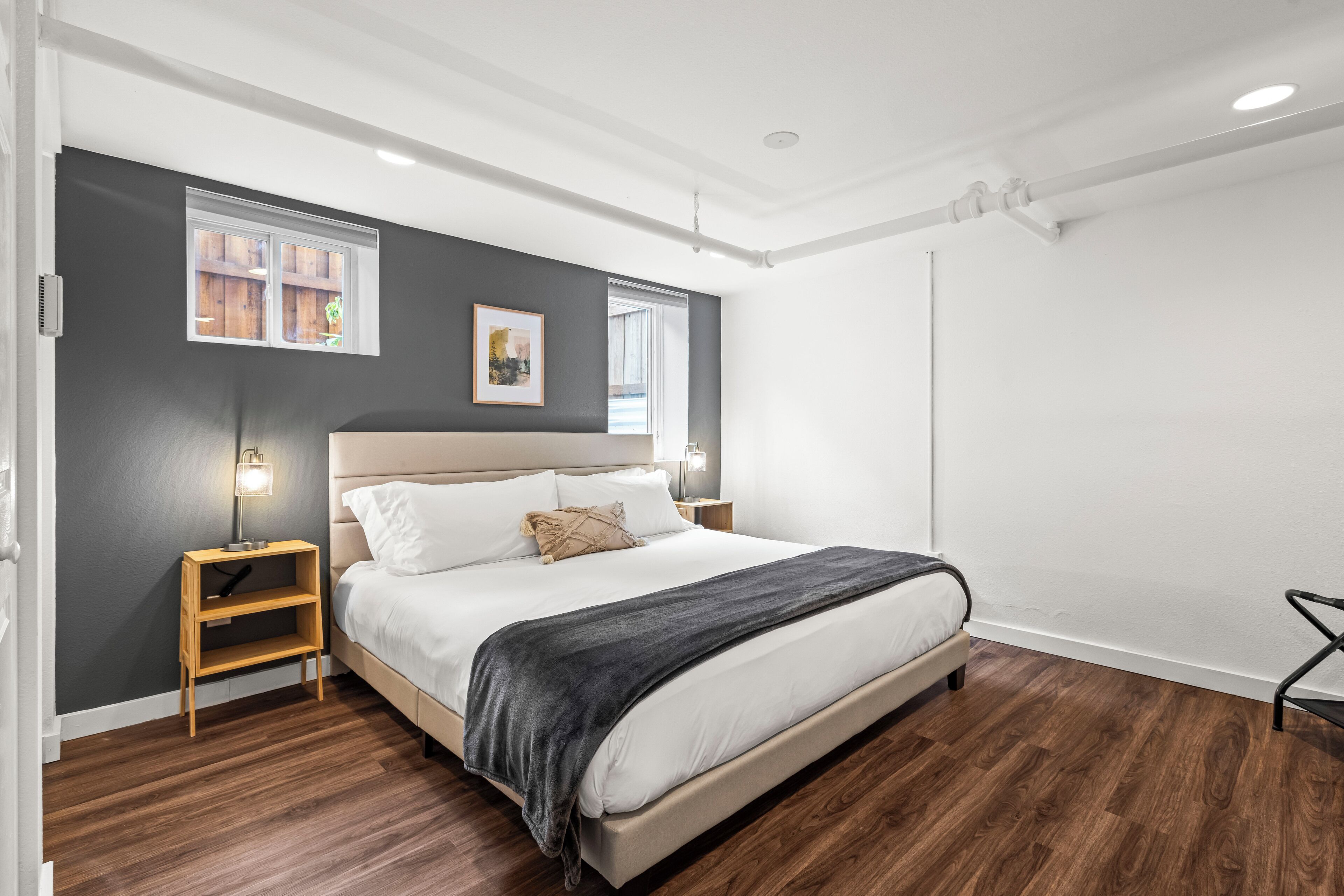 A modern bedroom with a large bed, wooden nightstands, a dark wall, and a window.