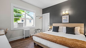 A modern bedroom with a large bed, a radiator, a window with blinds, a wall-mounted light fixture, and a framed picture. - 5280 Oasis - Hot Tub + Walk to Sloan's Lake (Denver)