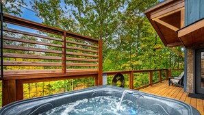 Un bain à remous sur une terrasse en bois, avec vue sur les arbres et un bâtiment.