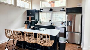 A modern kitchen with a central island, black cabinetry, stainless steel appliances, and wicker chairs. - Under 1 mile to Dollywd, 5 mins Pkwy - 2 Kings/2 BA - Small fam or couples (Pigeon Forge)