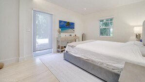 A modern bedroom with a large bed, a desk, and a window with a view of trees.