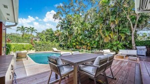 A wooden deck with a pool, outdoor furniture, and lush greenery.