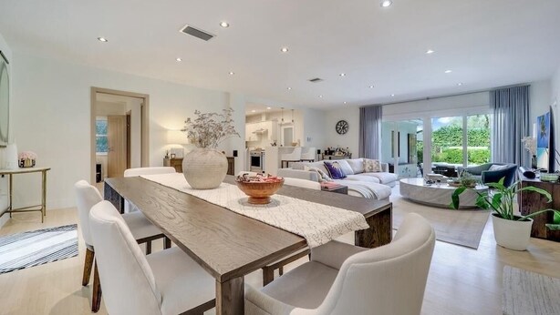 A spacious living area with a dining table, sofas, and a large window offering a view of greenery.