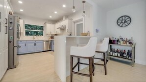 A modern kitchen with white cabinets, a central island with bar stools, and a wine rack.