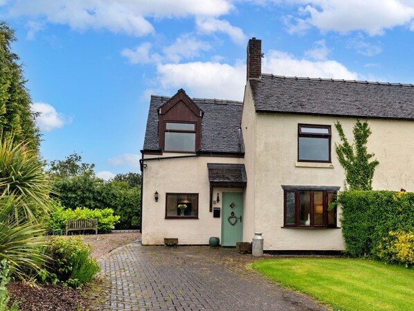 A two-story house with a paved driveway, a green door, and a small garden.
