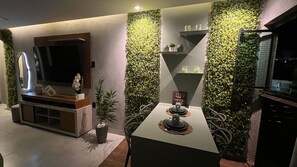 A modern living room with a flat-screen TV, a dining table with a decorative centerpiece, and vertical green wall panels. - Porto Esmeralda Apartment (Ipojuca)