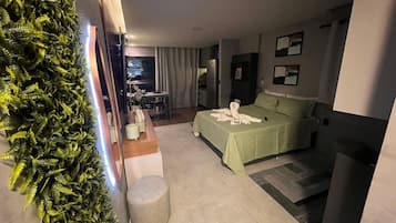 A hotel room with a bed, a desk, a chair, a small table, and a plant.