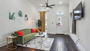 A living room with a green sofa, a coffee table, and a TV mounted on the wall.