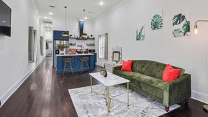 A modern kitchen with blue cabinets, a central island with stools, and a dining area with a green sofa and red cushions.