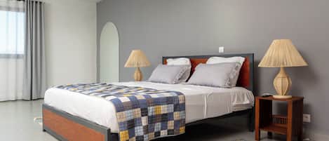 Un dormitorio moderno con una cama grande, dos lámparas de noche, una alfombra estampada y un ventanal con cortinas.