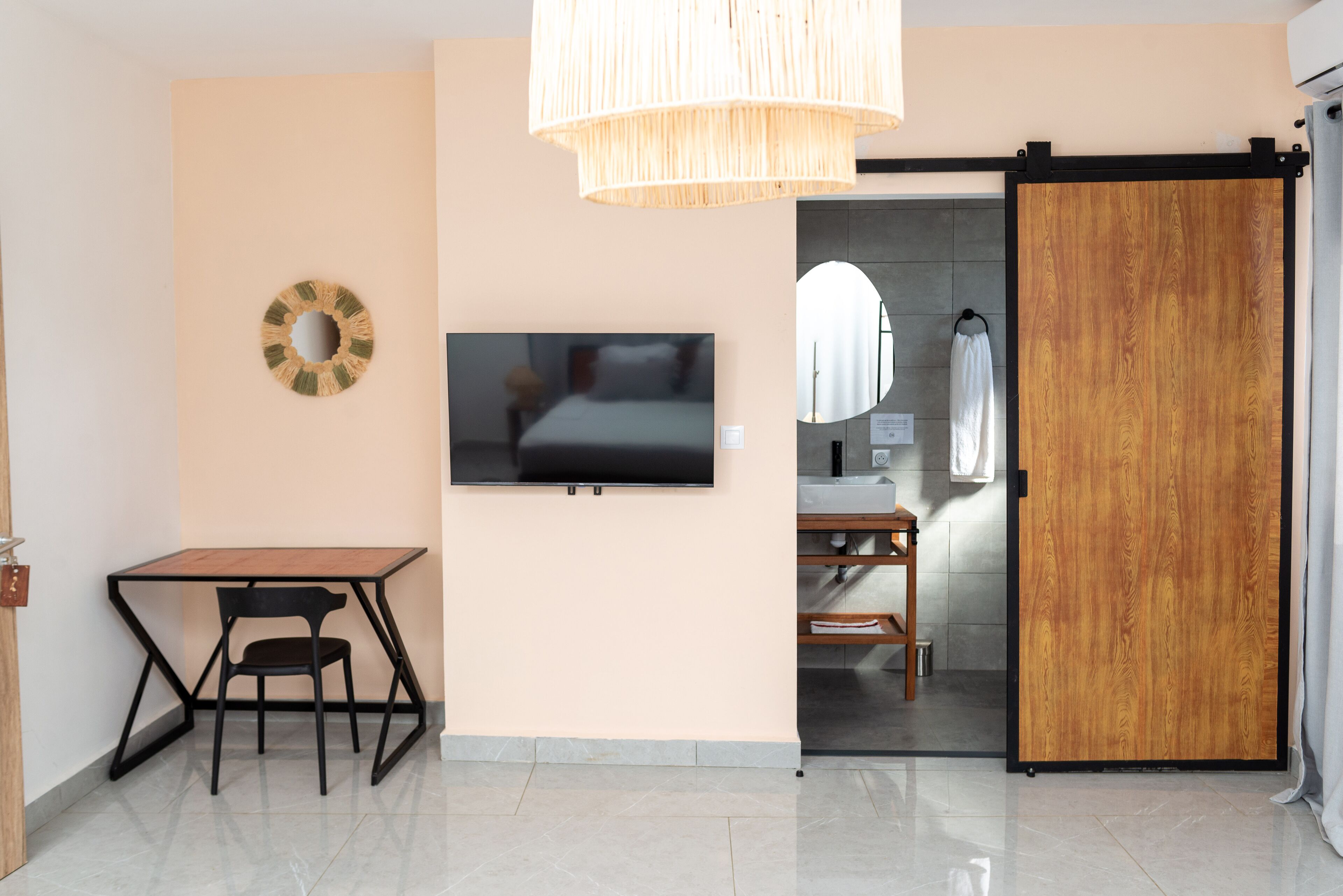 Una camera moderna con televisore, una porta in legno, un tavolo da pranzo con sedie e una lampada a sospensione.