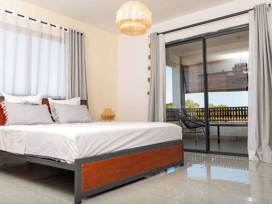 Un dormitorio moderno con una cama grande, un balcón con una silla y un ventanal corredero.