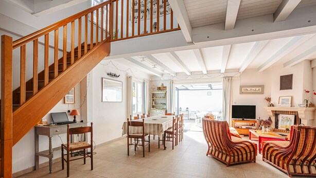 A spacious living area with a wooden staircase, a dining table with chairs, and a fireplace.