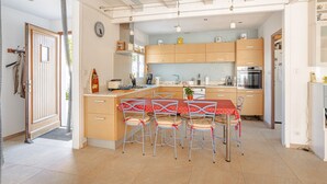 A modern kitchen with wooden cabinets, a central island, and a dining area with metal chairs.