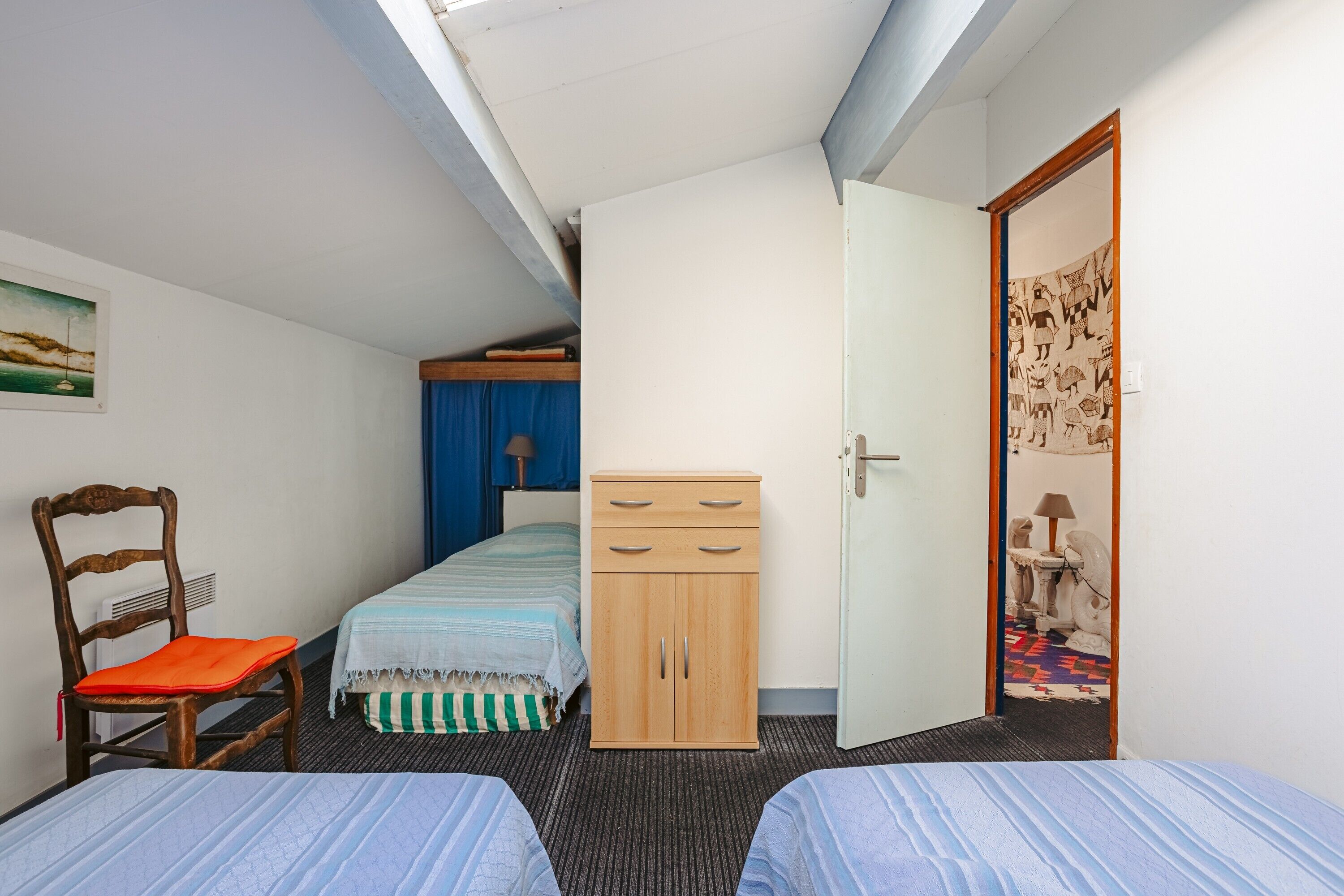 Un dormitorio con dos camas, un armario de madera, una silla y una puerta que da a otra habitación.