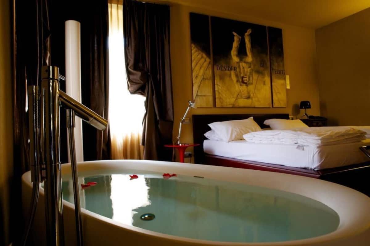 A hotel room with a large bathtub, a bed with neatly folded white linens, and a painting on the wall.