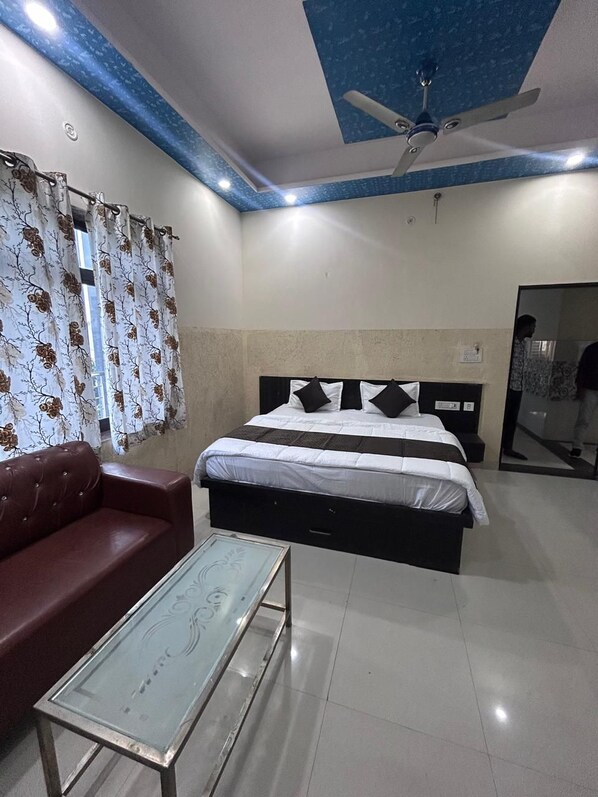 A bedroom with a bed, a red sofa, a glass coffee table, and a ceiling fan. - Hotel Tanwar (Jaipur)