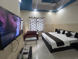 A hotel room with a bed, a sofa, a TV, and a window with curtains. - Hotel Tanwar (Jaipur)