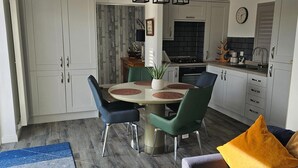 A modern kitchen with white cabinets, a round dining table with green chairs, and a blue rug.