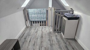 A loft bedroom with a sloped ceiling, grey wooden flooring, a white wardrobe, and a patterned rug. - 2 Bed Cottage-sleeps 4-harbour & Sea View (Peterhead)