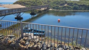 A bridge over a calm river with a rocky shoreline and a distant hill.