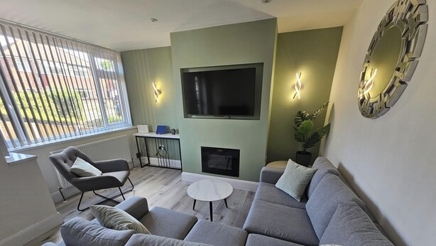 A modern living room with a grey sectional sofa, a small white table, and a TV mounted on the wall. - House - Sleeps 4 - Parking - Garden - City Centre (Leeds)