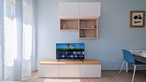 Un salon moderne avec un téléviseur à écran plat posé sur un meuble en bois, un meuble blanc en dessous et une chaise bleue sur la droite.