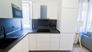 Une cuisine moderne équipée d’un four à micro-ondes, d’une cuisinière et d’un évier. On y trouve une fenêtre avec des rideaux, une petite table et une lampe.
