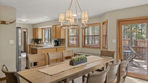 Una cocina amplia con armarios de madera y una isla grande, un comedor con mesa y sillas de madera, y vistas al exterior a través de amplias ventanas.
