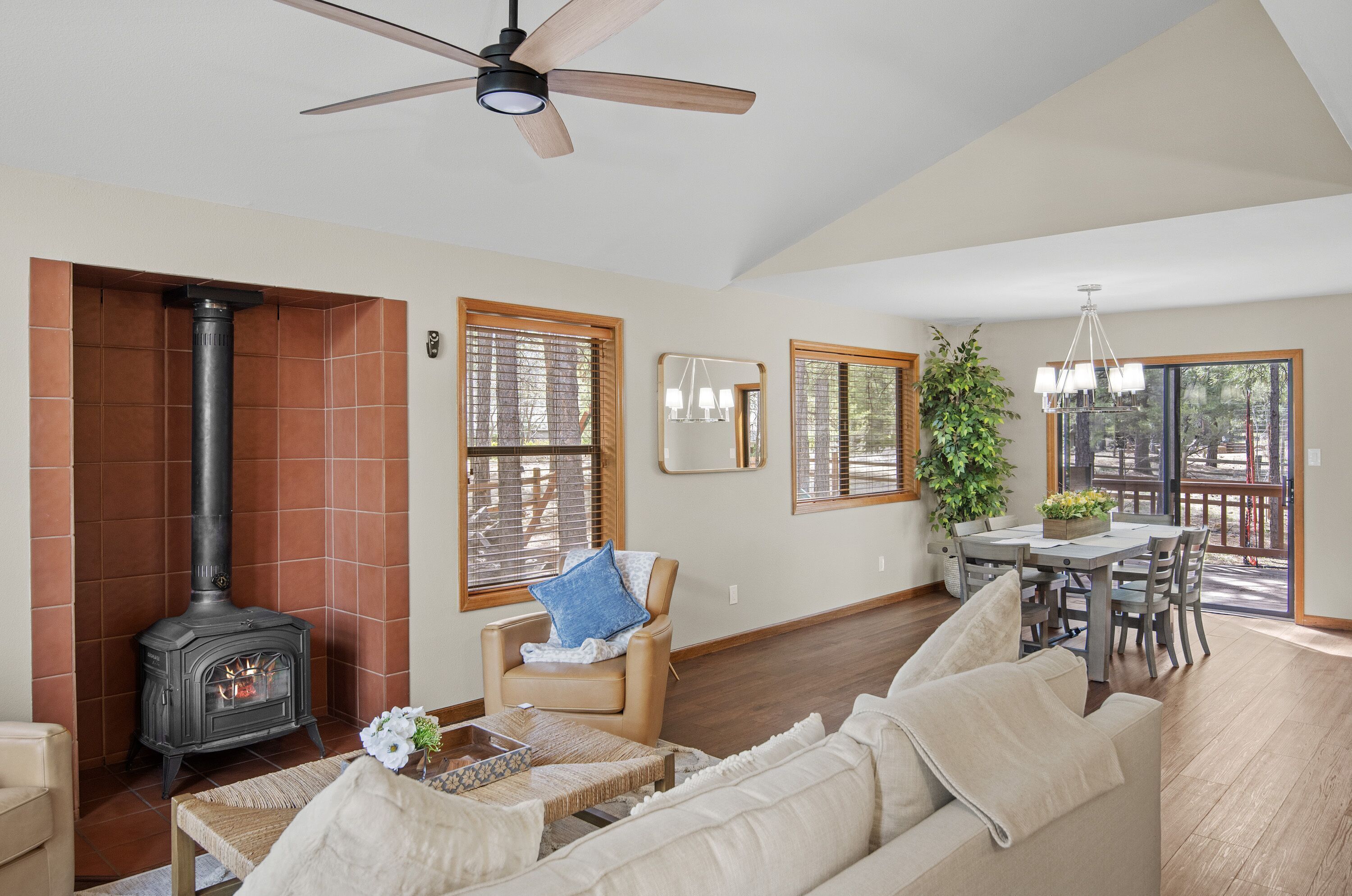 Una sala de estar con chimenea, ventilador de techo, comedor y ventanas amplias.