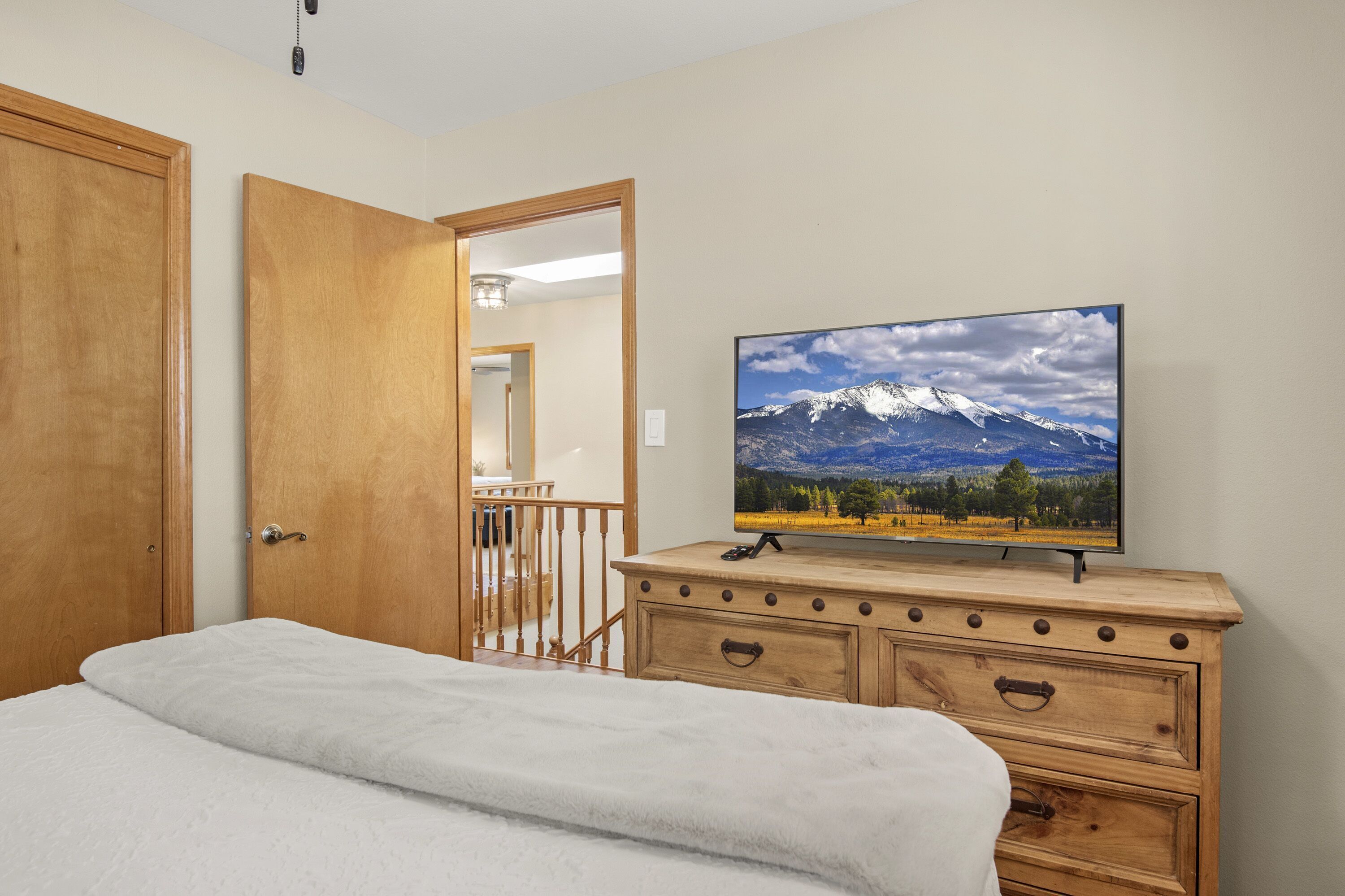 Een slaapkamer met een bed, een houten dressoir en een televisie waarop een berglandschap te zien is.