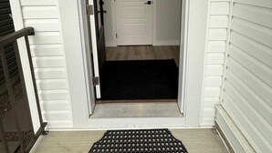 Une entrée de maison avec une porte blanche, un paillasson et une pancarte « Bienvenue » au-dessus de la porte.