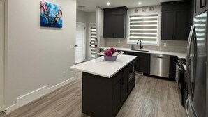 Une cuisine moderne dotée d’un îlot central, de meubles de couleur sombre, d’appareils électroménagers en acier inoxydable et d’un tableau accroché au mur.