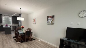 Un salon moderne avec un coin repas, une cuisine à l’arrière-plan et un meuble TV agrémenté d’objets décoratifs.