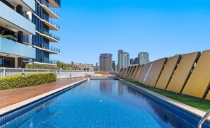 A modern swimming pool with a city skyline in the background, surrounded by high-rise buildings.