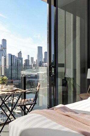 A modern hotel room with a large glass door leading to a balcony with a city view.
