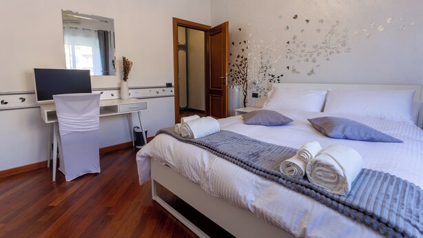 Une chambre d’hôtel comprenant un lit, un bureau avec une chaise, un miroir et un mur décoré de motifs de feuilles.