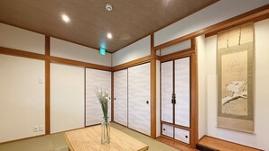 A traditional Japanese room with tatami flooring, a wooden table, a vase with flowers, sliding doors, and a framed artwork on the wall. - Wanoyado Kanayama (Hiroshima)