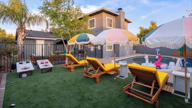Ein Garten mit Kunstgrasanlage, einem Swimmingpool, Liegestühlen und Sonnenschirmen.