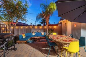 Une terrasse extérieure avec un canapé bleu, des chaises jaunes, une table ronde en bois et un barbecue.
