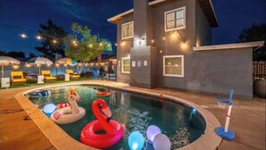 A swimming pool with inflatable swan and flamingo toys, surrounded by a building with a modern design and string lights. - This house is a 5 bedroom(s), 3 bathrooms, located in Phoenix, AZ. (Phoenix)