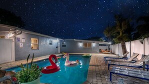 A swimming pool with a swan float and a unicorn float, surrounded by lounge chairs and palm trees.