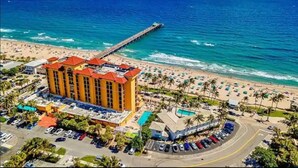 A hotel with a red roof, a pool, and a beach view.