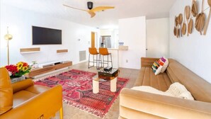A modern living room with a sofa, a coffee table, and a TV. There is a patterned rug on the floor.
