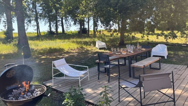 Un espace extérieur aménagé pour les repas, avec un barbecue, des chaises et une table dressée pour un repas.