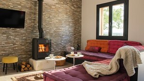 Un salon chaleureux avec un mur en pierre, une cheminée, un canapé, un téléviseur et une fenêtre donnant sur un beau paysage.